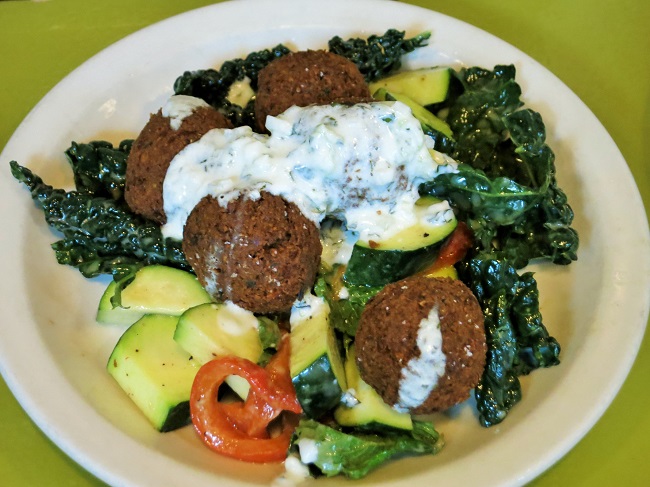 Crispy chickpea falafel on a salad of zucchini, kale, roasted peppers, preserved lemon, mint, with sauce blanche.