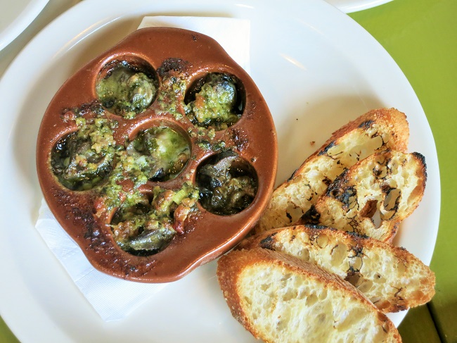 Burgundy snails baked with green garlic, jambon de Bayonne, walnut oil and butter, served with grilled baguette slices.